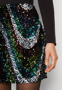 Mini-jupe en sequins noirs présentant un motif en vagues avec des sequins verts, bleus et argentés. Texture lisse avec une coupe ajustée.