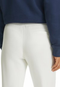 Weiße Hose mit strukturierter Oberfläche, ausgestattet mit einer Seitentasche und einem elastischen Bund, kombiniert mit einem navyblauen Sweatshirt.