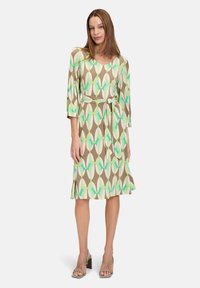 Braunes Kleid mit einem geometrischen Muster in Weiß, Grün und Hellblau. Mit V-Ausschnitt, dreiviertel Ärmeln und einem Taillengürtel.