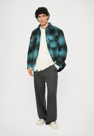 Camicia di flanella a quadri turchese e nera, maglione bianco a trecce, pantaloni grigi a gamba larga e sneakers avorio. Look testurizzato e stratificato.