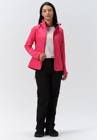 Pink waterproof jacket with high collar, zip closure, and black lining. Paired with black zip-off pants and black sports shoes.