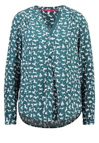 Teal blus med v-ringning, prydd med ett vitt hundmönster, långa ärmar och knappdetaljer. Mjuk tyg med avslappnad passform och rundad nederkant.