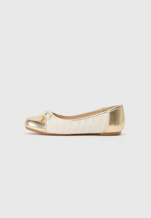Bailarina de tejido crema con patrón embossado, punta metálica dorada y lazo decorativo. Textura suave con suela flexible.