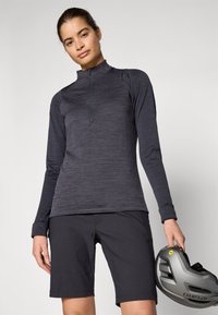 Mørkegrå, teksturert genser med lange ermer og kvart glidelås, kombinert med matchende shorts; holder en grå sykkelhjelm med gule detaljer.
