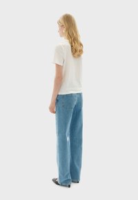 White short-sleeve t-shirt paired with light blue, wide-leg jeans. The jeans feature classic back pockets and a loose fit. Black shoes complete the outfit.