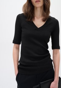 Svart randig V-ringad topp med korta ärmar, med en figurnära design och slät textur. Matchad med svarta byxor och en svart clutch.