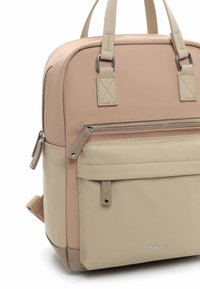 Sac à dos beige et marron clair avec poche avant zippée, double poignée supérieure, fermeture éclair latérale et détails cousus.