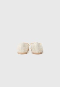 Chaussures slip-on crème texturées avec un design tissé, une forme élancée et des semelles minimalistes couleur sable. Pas de matériel ou d'accents visibles.