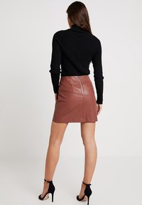 Mini-jupe en cuir marronavec une texture lisse et une fermeture éclair au dos, associée à un col roulé noir ajusté en maille côtelée et des chaussures à talons noirs.