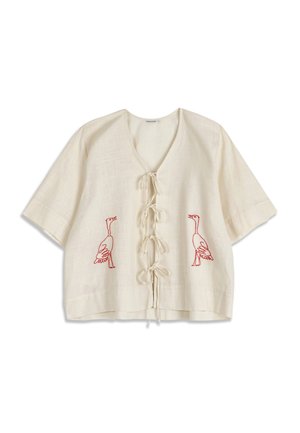 Kerma-valkoinen lyhythihainen pusero, jossa edessä solmittavat nauhat ja kummallakin puolella punaisella kirjailtuja hanhien kuvioita.