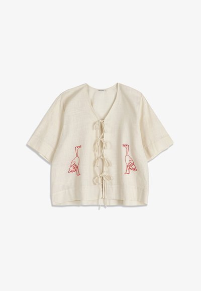 Blouse crème à manches courtes avec liens à l'avant et motifs brodés d'oies rouges de chaque côté.