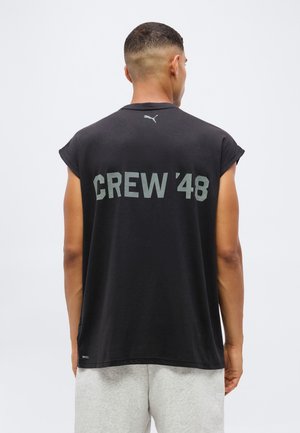 Homme vu de dos portant un débardeur noir avec "CREW '48" en texte gris et un petit logo Puma au niveau du cou, associé à un short gris clair.