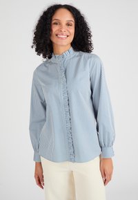 Lichtblauw en wit gestreept overhemd met een gerimpelde stolpplooi, hoge kraag en lange mouwen, gecombineerd met crèmekleurige broek.