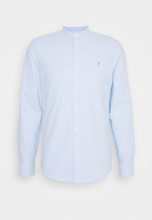 Hellblaues Langarmhemd mit Stehkragen, Frontknöpfen und kleinem gelben Logo auf der Brust. Baumwollmaterial, glatte Textur.