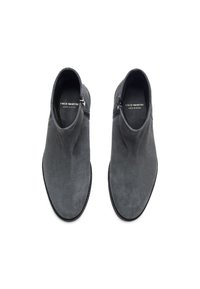 Bottines en suède gris avec une texture lisse, fermeture éclair sur le côté et une forme de orteil effilée. Étiquette indique "FRED MARTIN, FABRIQUÉ EN ESPAGNE."