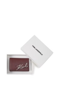Bordeaux leren portemonnee met zilveren "Karl" handtekening, gepresenteerd in een witte doos met zwarte merknaam. Compacte rechthoekige vorm, gestructureerde afwerking.