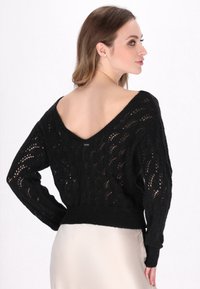 Schwarzer gestrickter Pullover mit V-Ausschnitt und Lochmuster, mit langen Ärmeln und geripptem Saum. Weiche Textur und leicht verkürztes Design.
