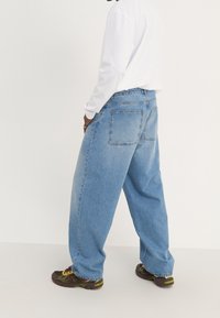 Ljust blå, högmidjade baggy jeans med en slät denimtextur, med två bakfickor och en rak benform. Stylade med svarta och gröna sneakers.