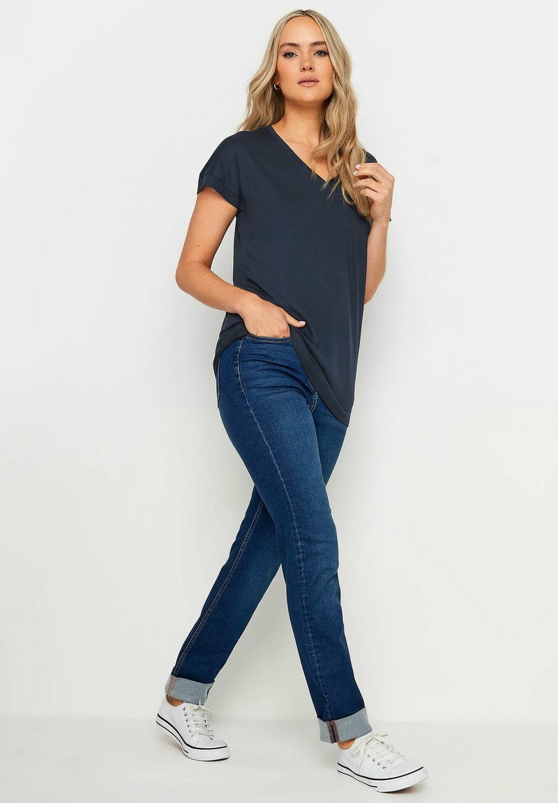 Tummanharmaa V-kauluksellinen lyhythihainen t-paita, yhdistettynä slim-fit sinisiin farkkuihin ja valkoisiin lenkkareihin, joissa on mustat raidat pohjassa.