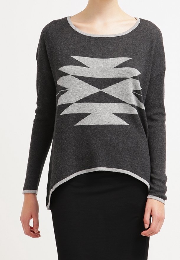 Pull gris foncé à manches longues avec un motif géométrique gris clair sur le devant, porté avec une jupe noire, modèle présenté du cou aux hanches.