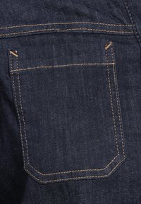 Tessuto di denim blu scuro con una tasca a filetto e cuciture arancioni, caratterizzato da una superficie liscia che mette in evidenza i dettagli costruttivi.