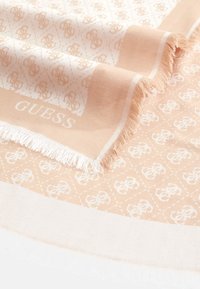 Jasnopomarańczowy szal z miękkiego materiału, z powtarzającym się białym wzorem logo, z frędzlami na krawędziach oraz jednolitą białą ramką.