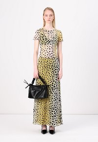 Abito lungo e trasparente con macchie di leopardo nere e gialle, con maniche corte. Borsa nera con manico intrecciato, abbinata a scarpe nere a punta.