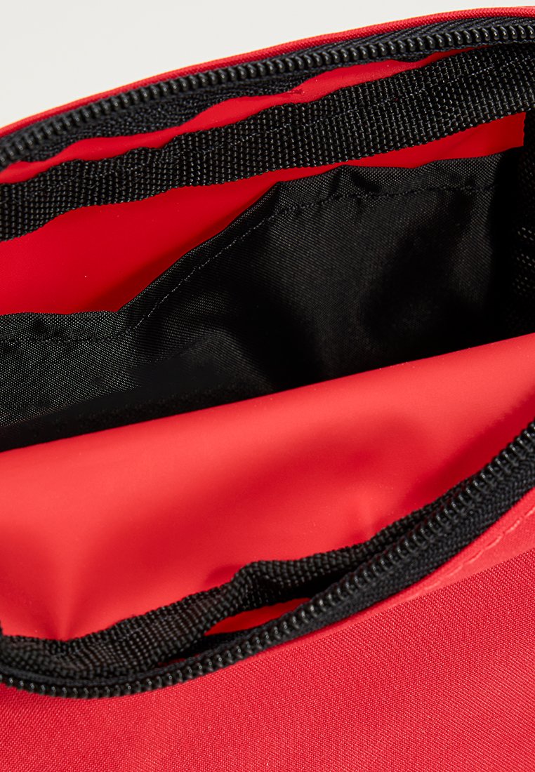 Interior de una bolsa de tela roja con un forro rojo liso y un bolsillo de malla negra en la parte superior. Presenta un zipper negro a lo largo del borde.