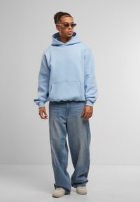 Lys blå hettegenser med frontlomme, paret med løstsittende lyse denimbukser og hvite sneakers. Minimalistiske designdetaljer.