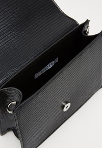 Borsa nera a trama con motivo a coste, ferrature argentate e chiusura a scatto. L'interno è foderato in tessuto e presenta un'etichetta.