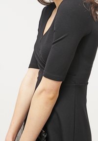 Czarna dopasowana sukienka z głębokim dekoltem w kształcie litery V i krótkimi rękawami. Wykonana z elastycznego materiału, charakteryzuje się gładką fakturą i dopasowanym krojem.