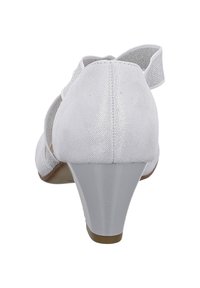 White suede low-heeled shoes with a rounded toe, featuring a silver accent on the heel and an open design with a strap at the back.