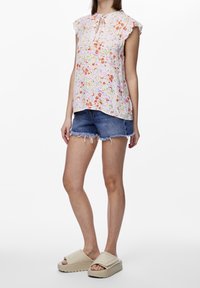 Koszula z krótkim rękawem w kwiatowy wzór w jasnoróżowym kolorze, z dekoltem w łezkę, zestawiona z przetartymi dżinsowymi szortami i beżowymi klapkami na koturnie.