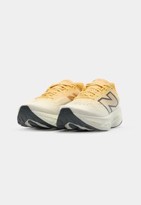 Žluté a krémové běžecké boty s prodyšným svrškem, texturovaným designem a černou gumovou podrážkou; na botách je šedé logo New Balance.