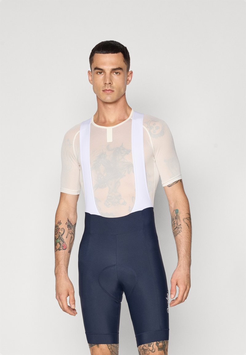 Conjunto de ciclismo que incluye una camiseta blanca de malla con mangas cortas y un short tipo tirantes azul marino. La tela es suave, tiene un diseño ajustado y no presenta patrones.