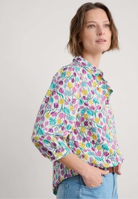 Camisa floral colorida con un fondo color turquesa claro, patrones de tulipanes en rosa, amarillo y verde, cierre de botones y mangas dobladas.