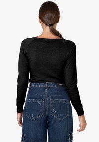 Top nero a maniche lunghe con scollatura rotonda, abbinato a jeans in denim strappati a vita alta con tasche applicate.