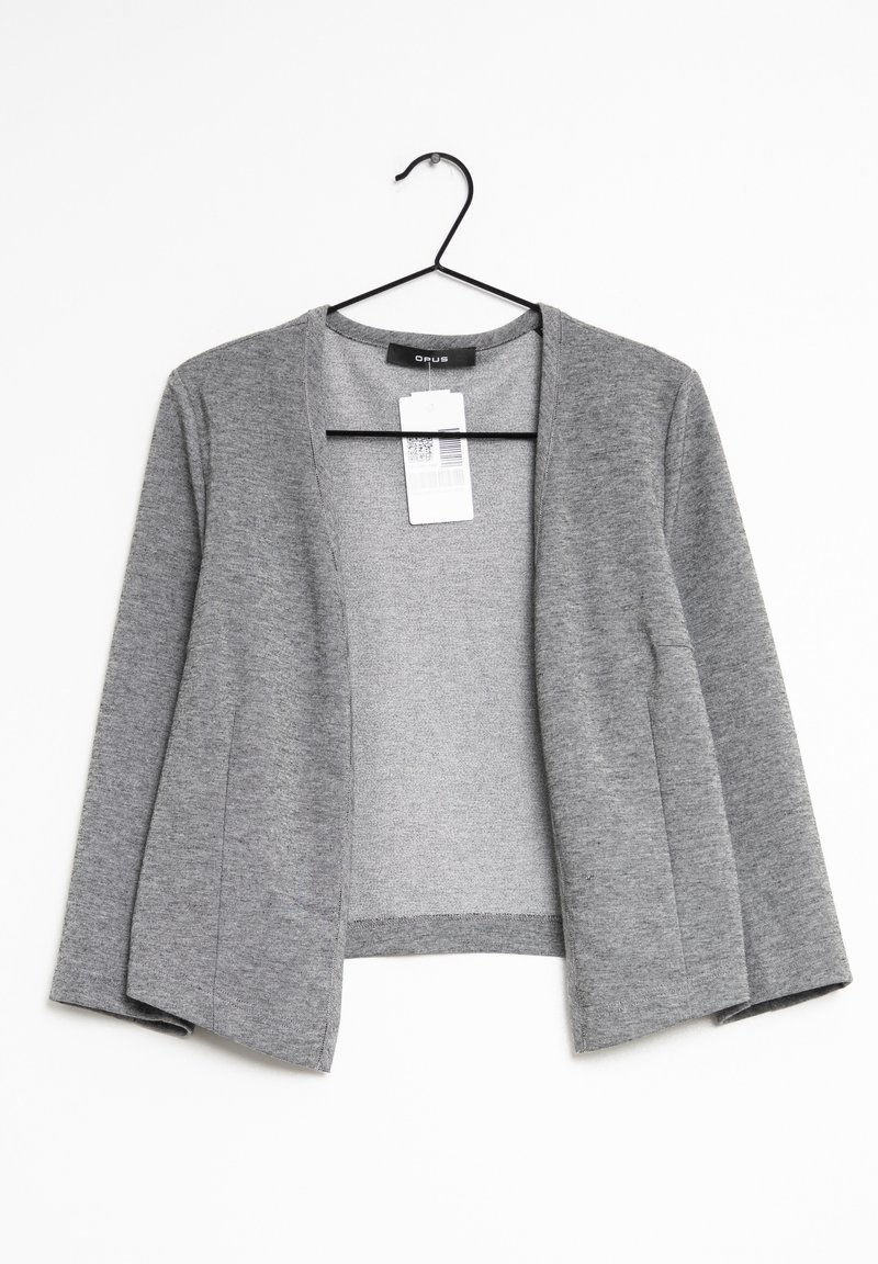 Grå kardigan i mjukt tyg, med öppen framsida, långa ärmar och utan knäppningar. Hänger på en svart plastgalge.