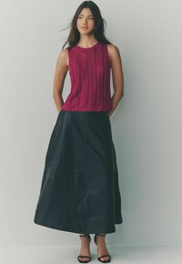 Fuchsia gestricktes ärmelloses Oberteil mit geripptem Muster, kombiniert mit einem schwarzen Leder-Maxikleid mit ausgestelltem Schnitt und vertikalen Nähten.