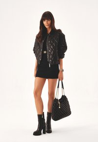 Black quilted bomber jacket, black mini dress, knee-high black heeled boots, and a black quilted handbag with chain straps.