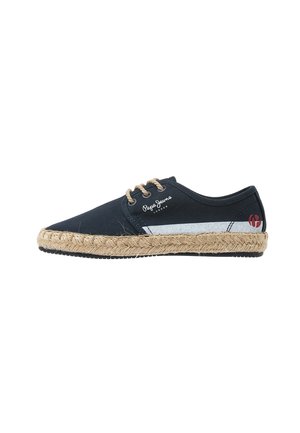 Espadrille de lona azul marino con suela de cuerda de yute, costuras beige y detalle de raya blanca. Presenta un logo de la marca en el lado exterior.