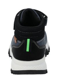 Zapato negro y gris de media caña con un cuello acolchado, entresuela blanca y una franja de acento verde en la parte trasera, con materiales texturizados y un diseño robusto.