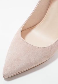 Escarpin en suède rose clair avec bout pointu et empeigne basse, présentant des détails de couture le long du bord et une doublure intérieure lisse.