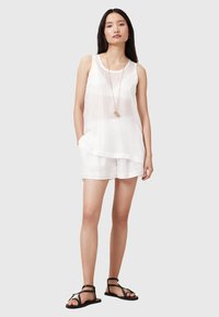Top bianco senza maniche e pantaloni corti abbinati realizzati in tessuto leggero, con orlo a strati. Abbinato a sandali neri flats e una collana lunga.