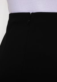 Musta, sileä kangas, jossa on vetoketjukiinnitys vyötäröllä. Hameessa on vartaloa myötäilevä muotoilu ja minimalistinen tyyli ilman näkyviä kuvioita.