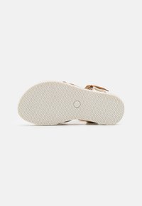 Suola di calzature con motivo a onde, colore beige chiaro e bordi arrotondati; rinforzata con una soletta imbottita per il comfort.