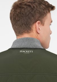 Tume roheline tikitud jope, halli soonilise kraega. "Hackett London" logo trükitud valge värviga seljaosal. Sile tekstuur, loodud täpseteks mõõtudeks.