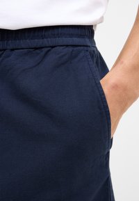 Shorts de tela azul marino con cintura elástica. Bolsillo lateral visible, que muestra un diseño simple y casual. Textura suave.