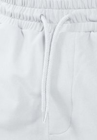 Gros plan sur la taille d'un pantalon de jogging blanc avec bande élastique et cordon tressé blanc noué à l'avant.