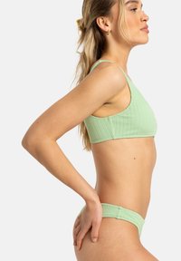 Jasnozielony bikini w prążki składający się z topu bez rękawów z szerokimi ramiączkami oraz pasujących dolnych części o niskim stanie, prezentujący teksturowany materiał.